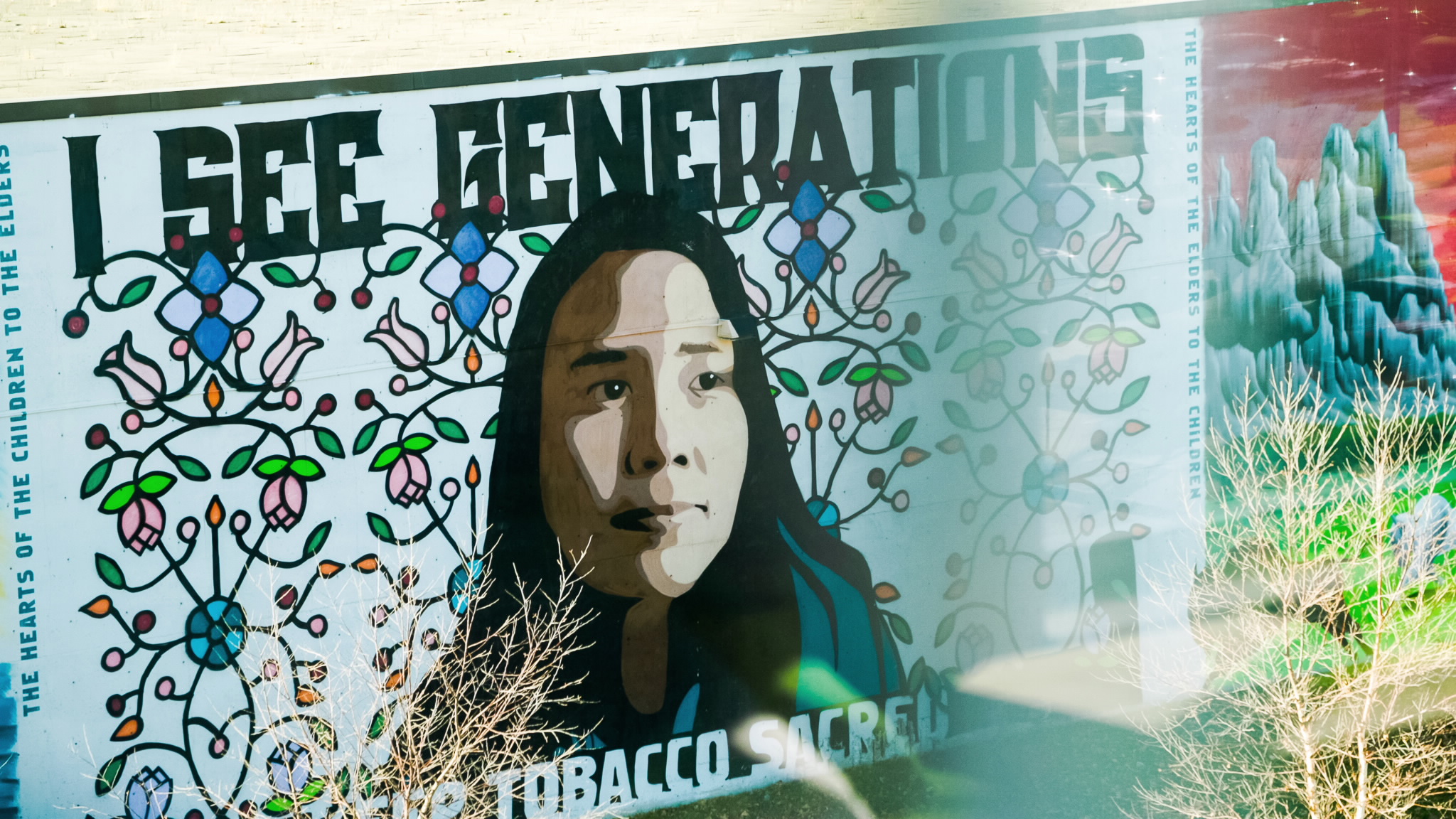 Community mural with a girl, flowers, and text, " I see generations. the heats of the elders to the children".